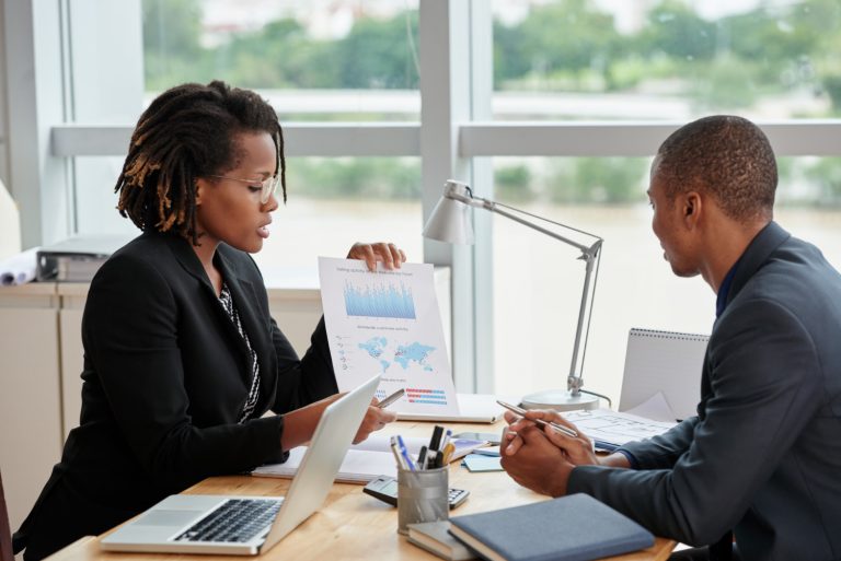 Vue latérale d'une femme d'affaires montrant des graphiques analytiques à son collègue masculin